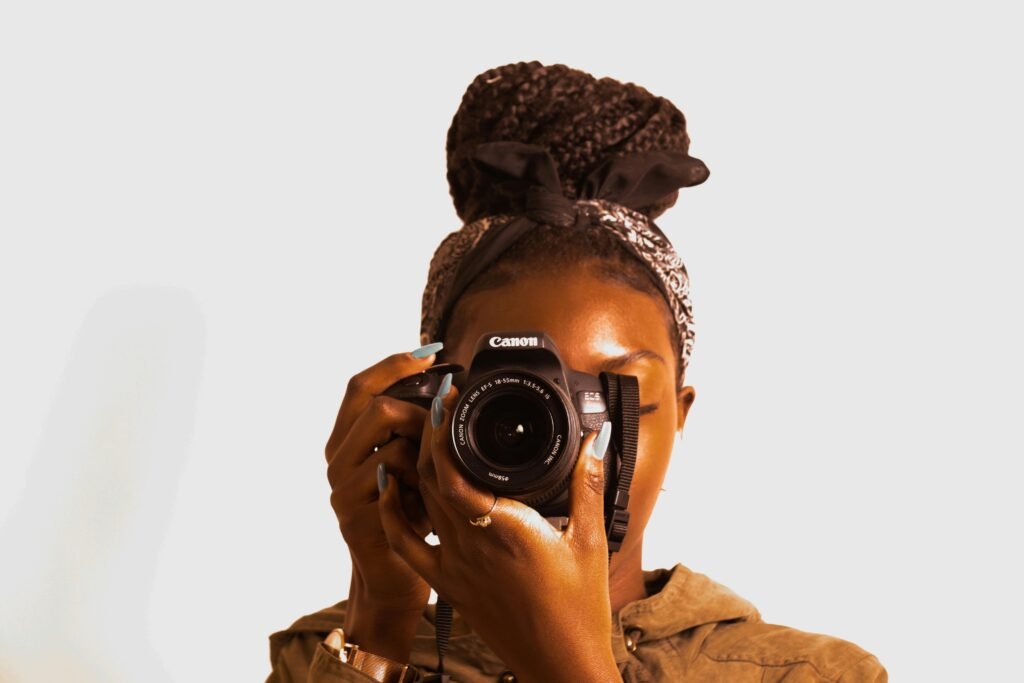 Portrait of a woman holding a DSLR camera with braided hair and bandana.